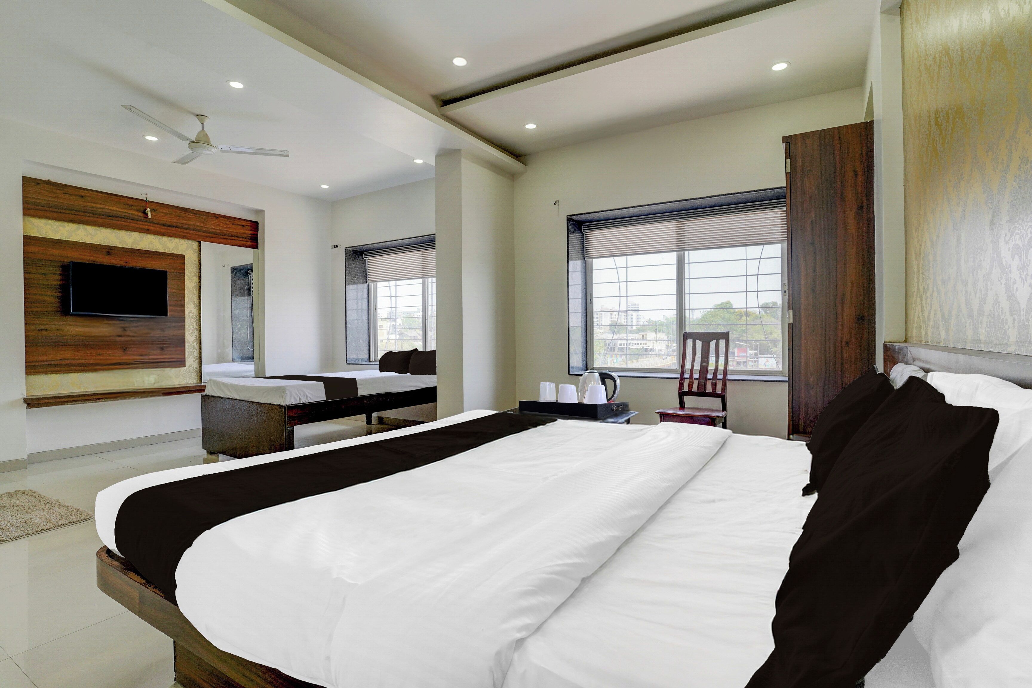 Habitación de hotel con una cama grande, un televisor de pantalla plana montado en la pared, una ventana con persianas y un ventilador de techo.
