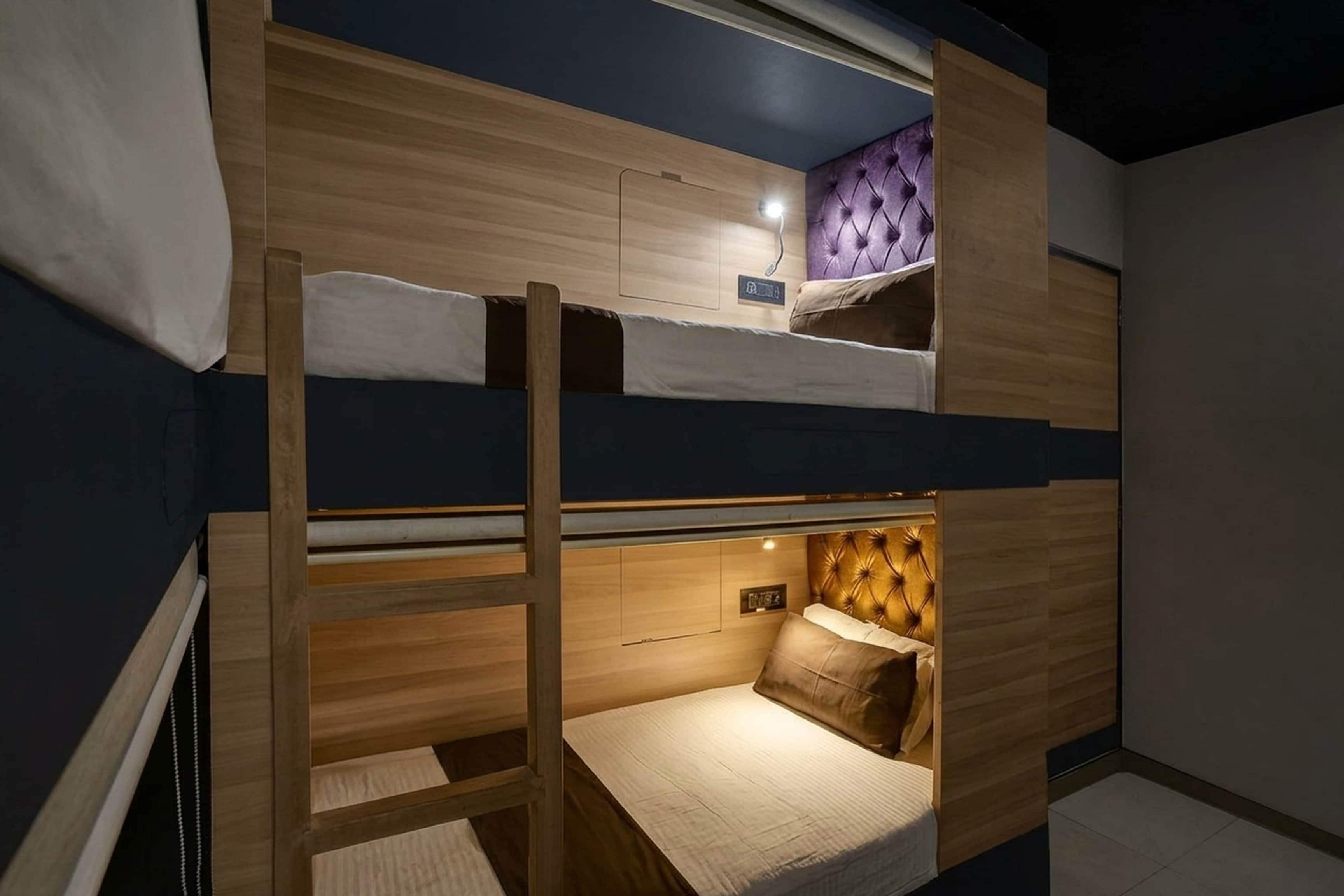 Habitación con literas, una escalera, cabecero y mesita de noche con lámpara.