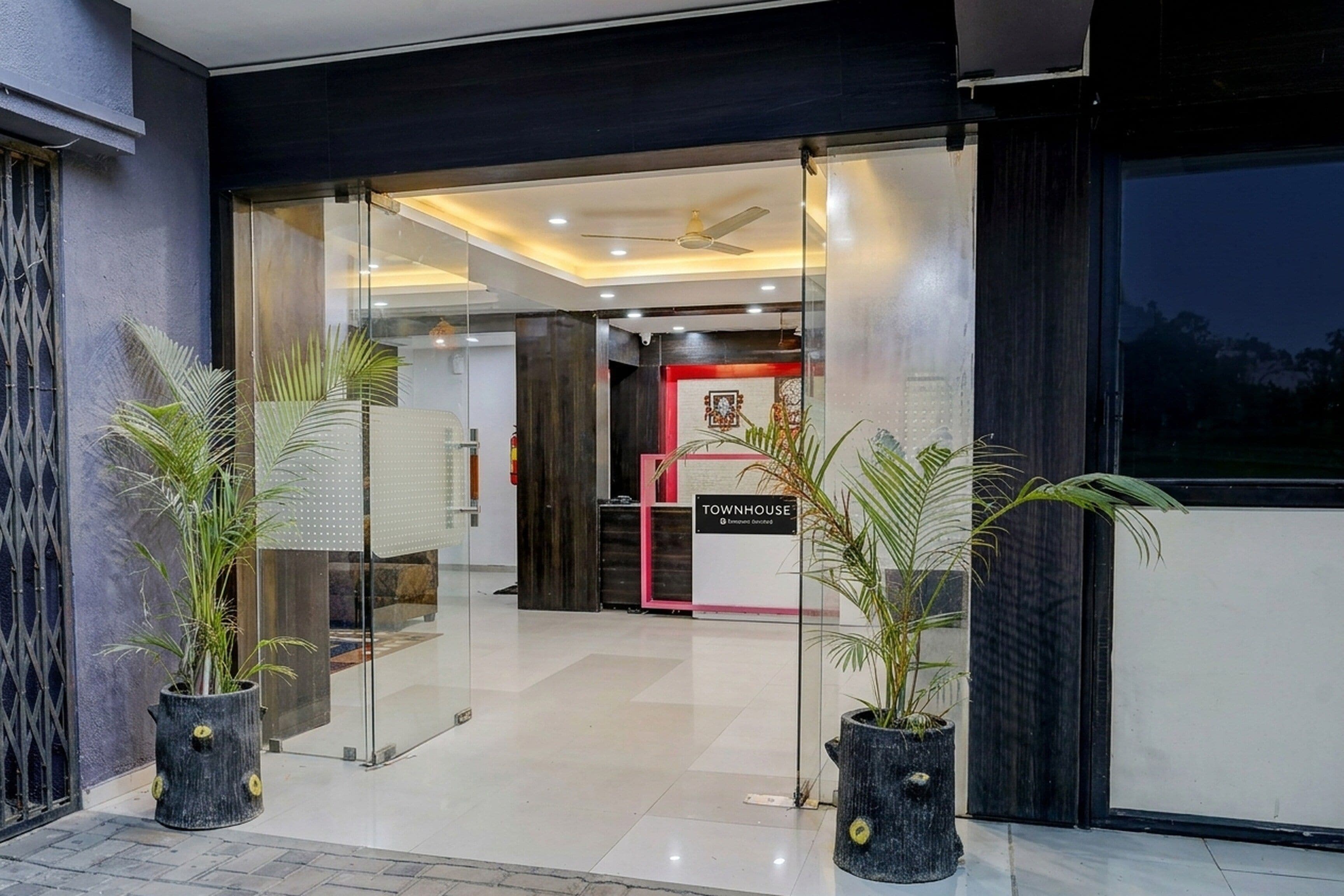 Una entrada de hotel moderna con puertas de vidrio, plantas en macetas y un letrero que dice 'TOWNHOUSE'.