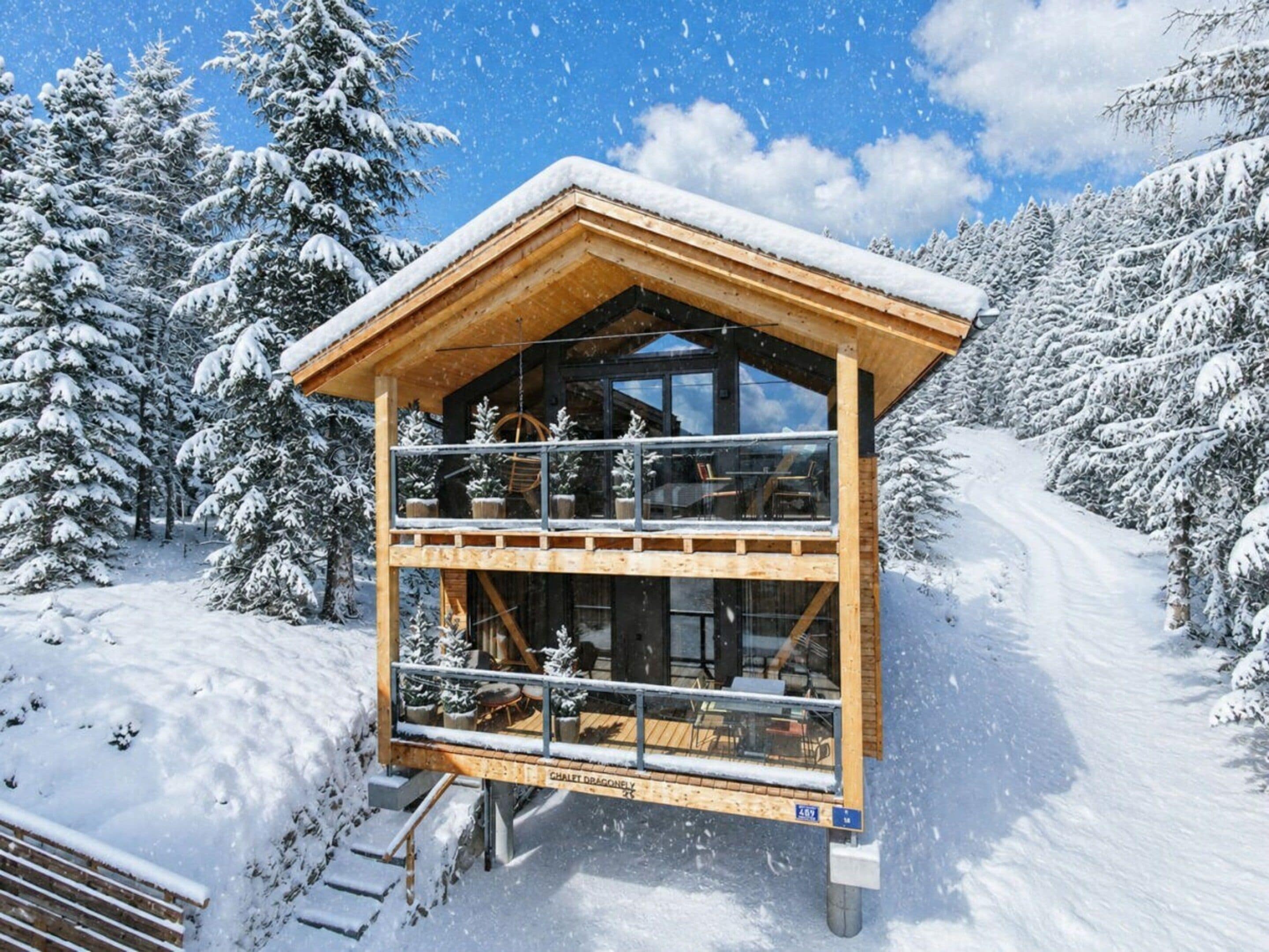 A wooden chalet with a balcony, surrounded by snow-covered trees.