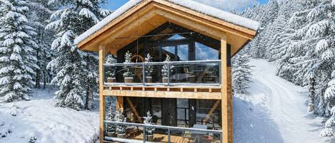 A wooden chalet with a balcony, surrounded by snow-covered trees.