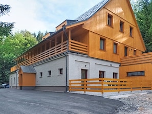 Un immeuble en bois à plusieurs étages, doté de balcons, d’un garage et d’une allée bordée d’une clôture.