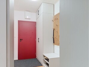 Un couloir avec une porte rouge, des placards blancs et un meuble à chaussures.