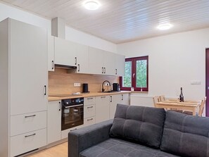 Une cuisine compacte dotée d’appareils électroménagers modernes, un coin repas avec une table et des chaises, et un canapé gris.
