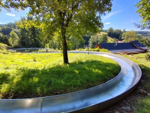 A metal slide in a grassy area with trees and a building in the background. - Cosy apartment for 4 guests with WIFI, TV, terrace and pets allowed (Jablonec Nad Nisou)
