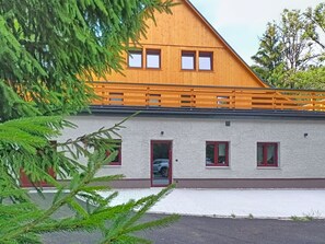 Ein zweistöckiges Gebäude mit einem geneigten Dach, einer Holzterrasse und einem gepflasterten Einfahrtsweg.
