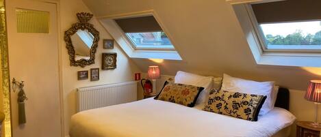 Een slaapkamer met een groot bed, dakramen, een kroonluchter en een radiator.
