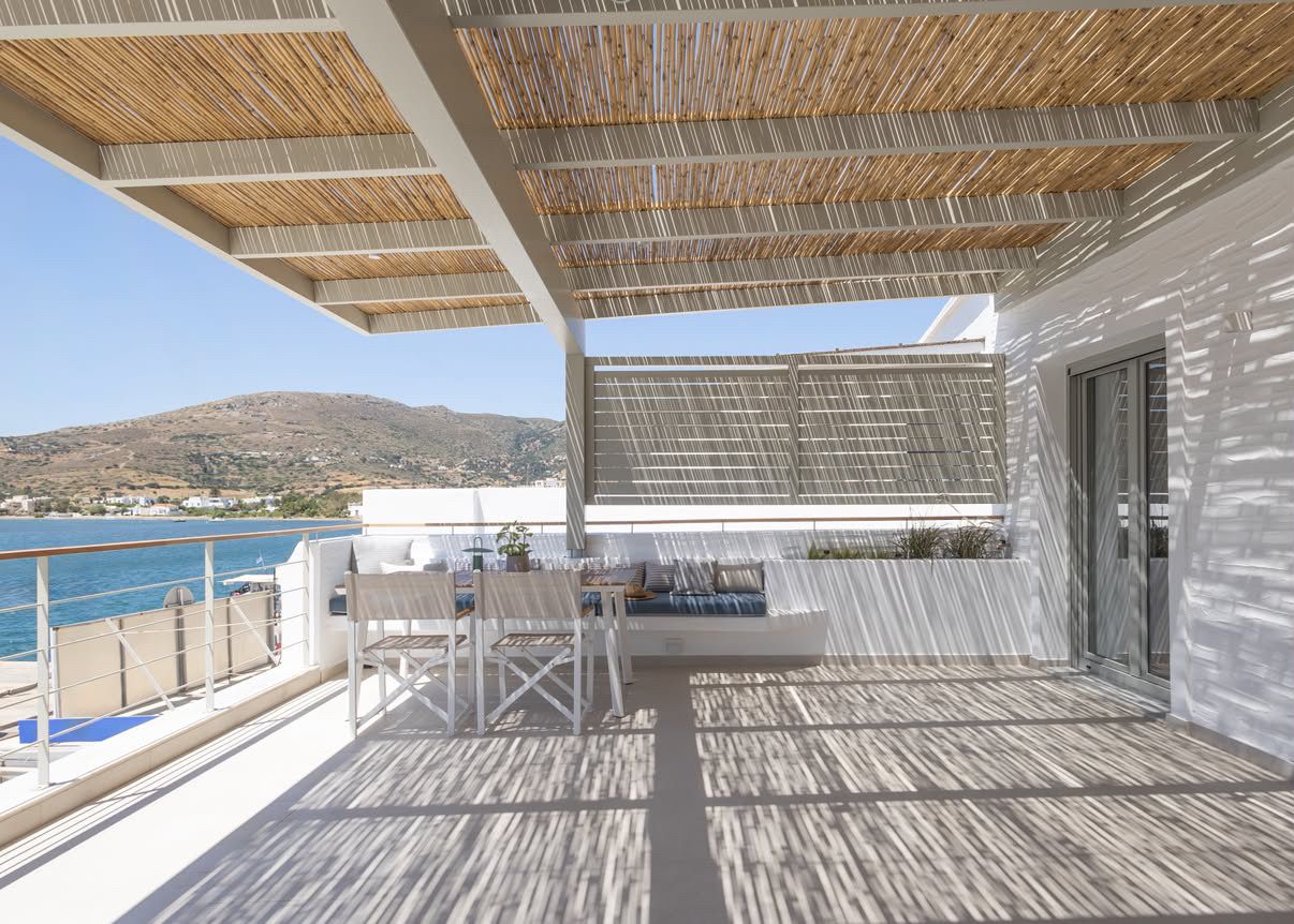 A balcony with a view of the sea and a mountain, featuring a table and chairs.