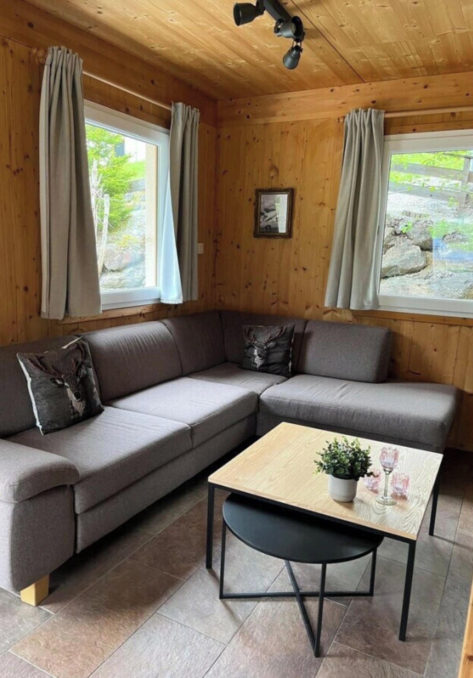 A cozy room with a sectional sofa, a small table with a plant and glasses, and a ceiling fan.