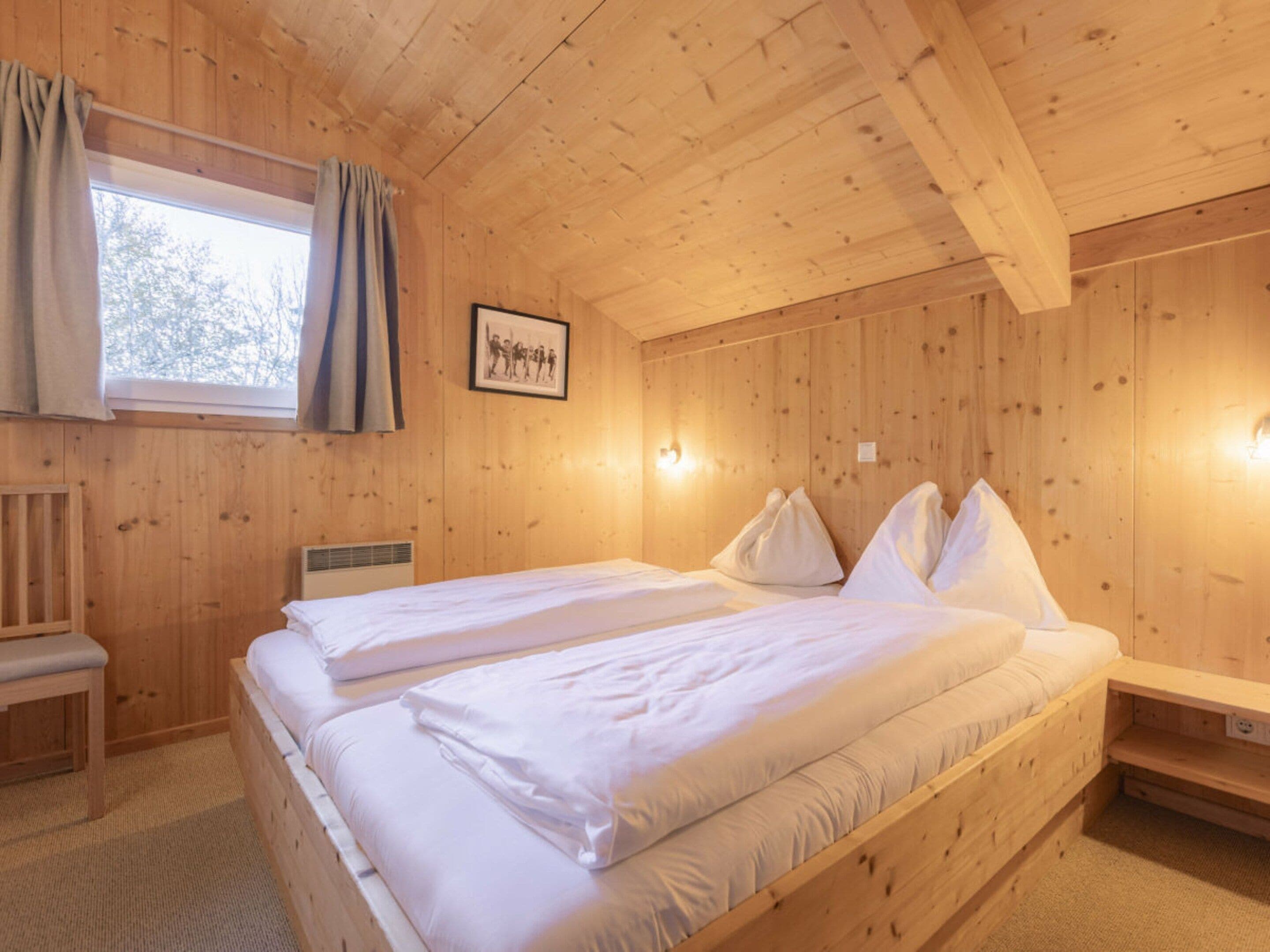 Une pièce de style cabane en bois, avec deux lits, un banc, une fenêtre avec des rideaux et un tableau encadré au mur.