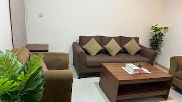 Una sala de estar con un sofá marrón, una mesa de centro de madera y una planta en maceta.
