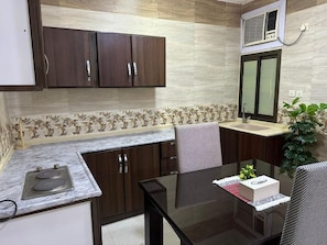 A compact kitchen with dark wooden cabinets, a marble countertop, and a glass dining table.