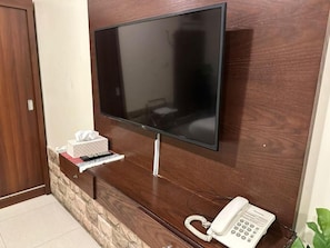 A flat-screen TV mounted on a wooden wall, a telephone, and a tissue box on a small shelf.