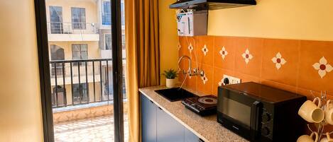 A compact kitchen with a microwave, a sink, and a stove. There's a window with a view of buildings outside.