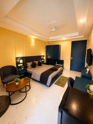 A modern bedroom with a bed, bedside tables, a chair, a desk, and a ceiling fan. - 5 Min to Medanta - Cozy 1 RK in Sector 38 (Gurugram)