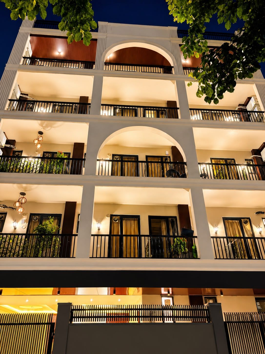Ein mehrgeschossiges Hotel mit Balkonen, Rundbogenfenstern und warmer Innenbeleuchtung.