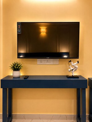 A flat-screen TV mounted on a wall with a remote control and a decorative sculpture on a blue console below. - 5 Min to Medanta - Cozy 1 RK in Sector 38 (Gurugram)
