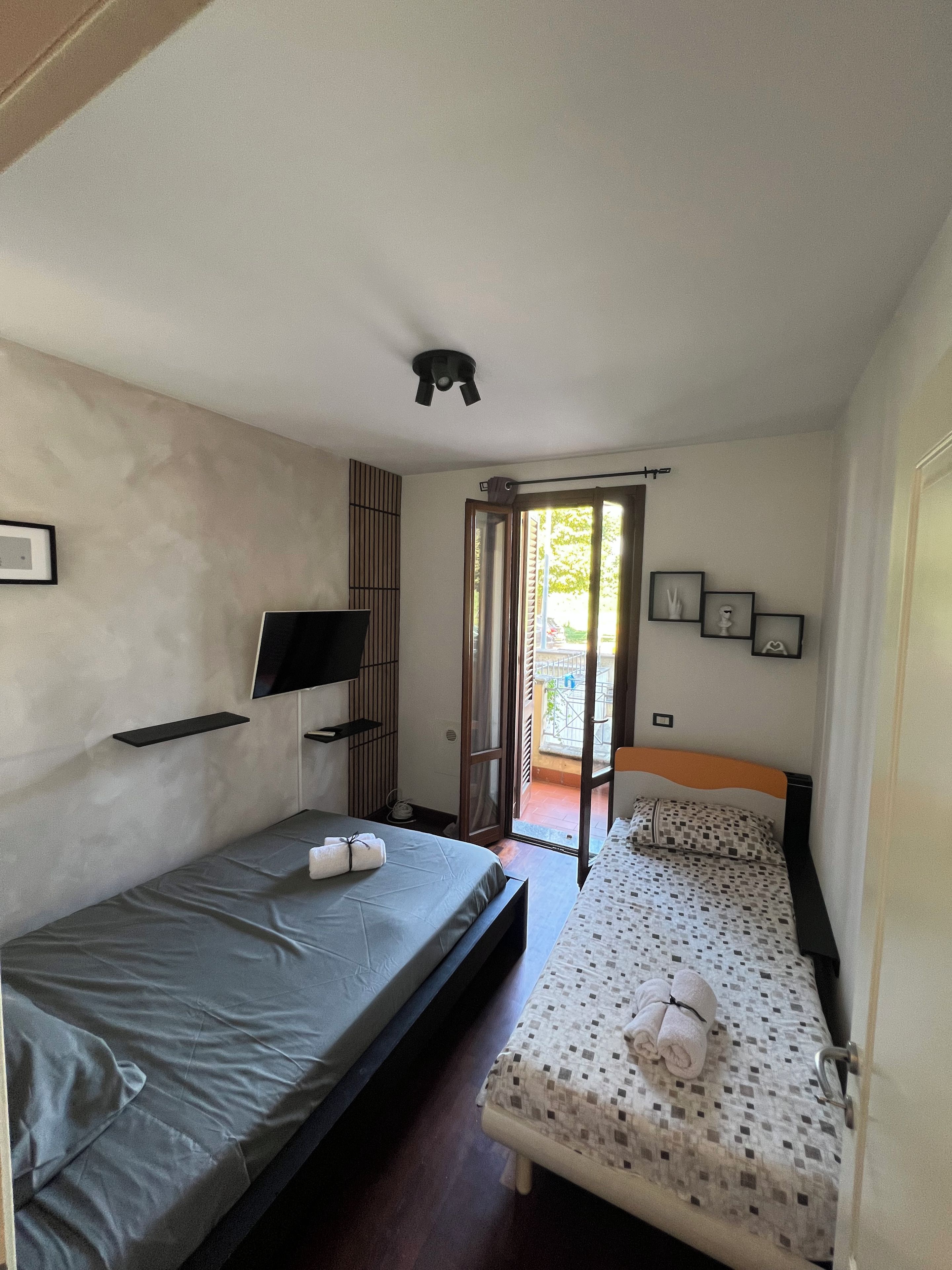 Una stanza con due letti, una TV, una lampada a soffitto e una porta che dà su uno spazio esterno.