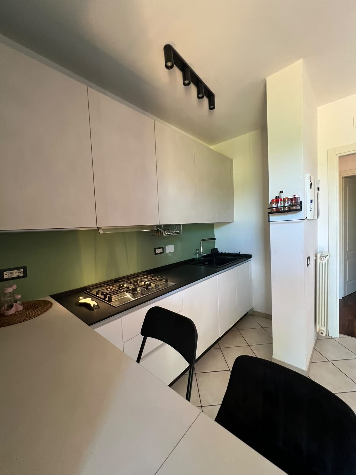 Una cucina moderna con mobili bianchi, un piano di lavoro nero e un piano cottura a gas.