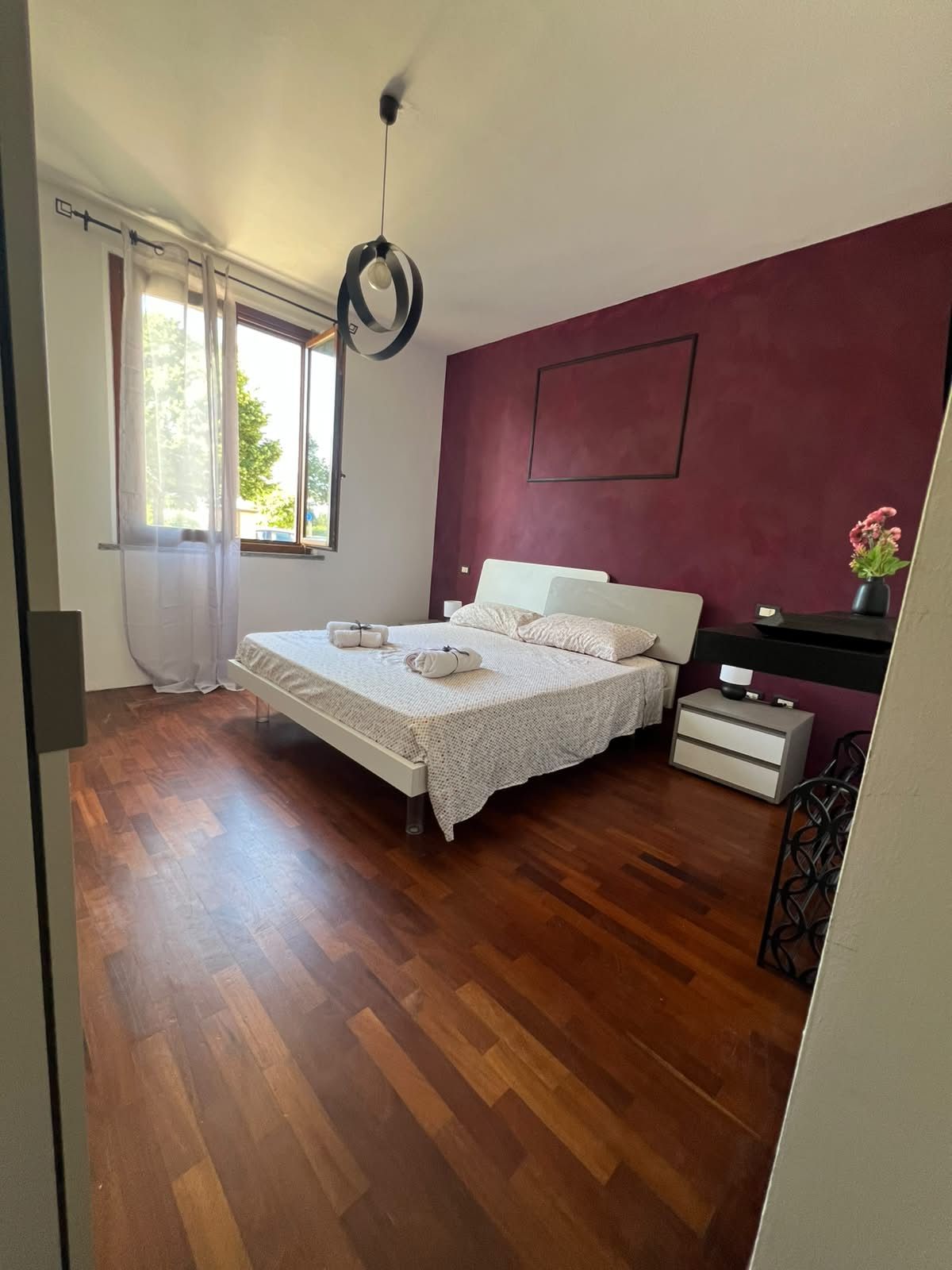 A bedroom with a bed, bedside tables, a window with curtains, and a hanging light fixture.