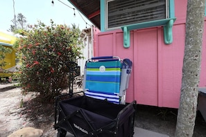 A beach chair with a striped cover and a black bag with 'EAKNOM' on it, placed outside a pink building with a window and a tree nearby. - PinkMango Cottage Steps to Beach&Village (Siesta Key)