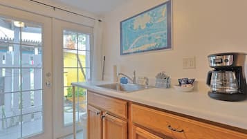 A kitchen with a white countertop, wooden cabinets, a coffee maker, and a window with a view of a yellow building.