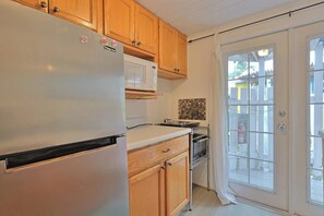 A kitchen with wooden cabinets, a white refrigerator, a microwave, and a sliding glass door leading outside. - PinkMango Cottage Steps to Beach&Village (Siesta Key)