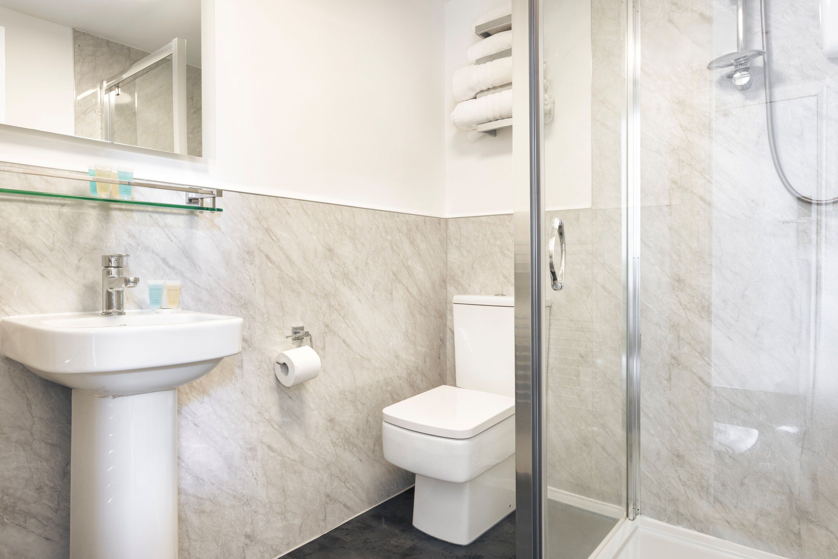 Un baño moderno con cabina de ducha de vidrio, un lavabo blanco y un inodoro.