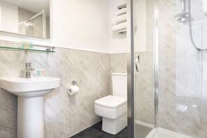 Un baño moderno con cabina de ducha de vidrio, un lavabo blanco y un inodoro.