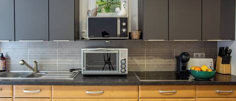 Una cocina con armarios grises, microondas, tostadora, un lavabo y un bol con fruta en la encimera.