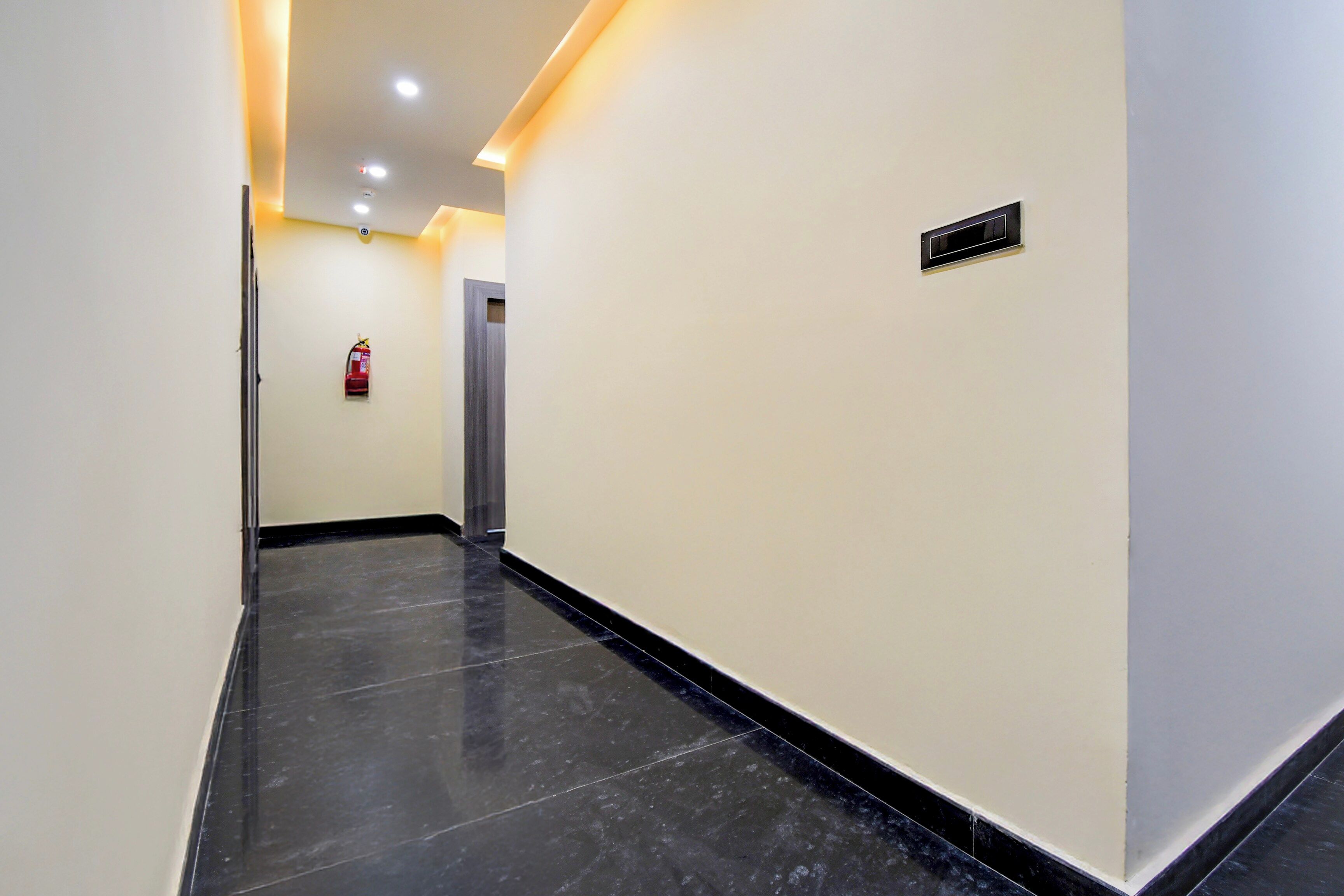 Un couloir avec un extincteur fixé au mur, une porte au fond et une grille d’aération sur le mur.