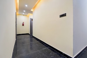 A corridor with a fire extinguisher mounted on the wall, a door at the end, and a vent on the wall.
