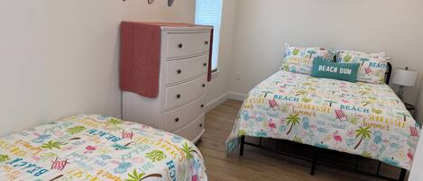 A bedroom with two beds, a ceiling fan, a dresser, and a window with blinds.