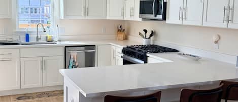 A modern kitchen with white cabinets, a stainless steel microwave, a large island with bar stools, and a window with a view of buildings.