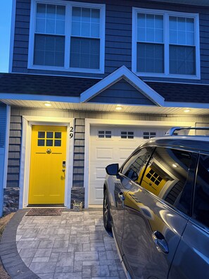 A house with a garage door, a yellow front door, and a parked car.