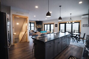 A modern kitchen with a large island, pendant lighting, and a view of the outdoors. - Luxury Mountain Escape • 6BR • Hot Tub & Views • 4mi to Sunday River (Bethel)