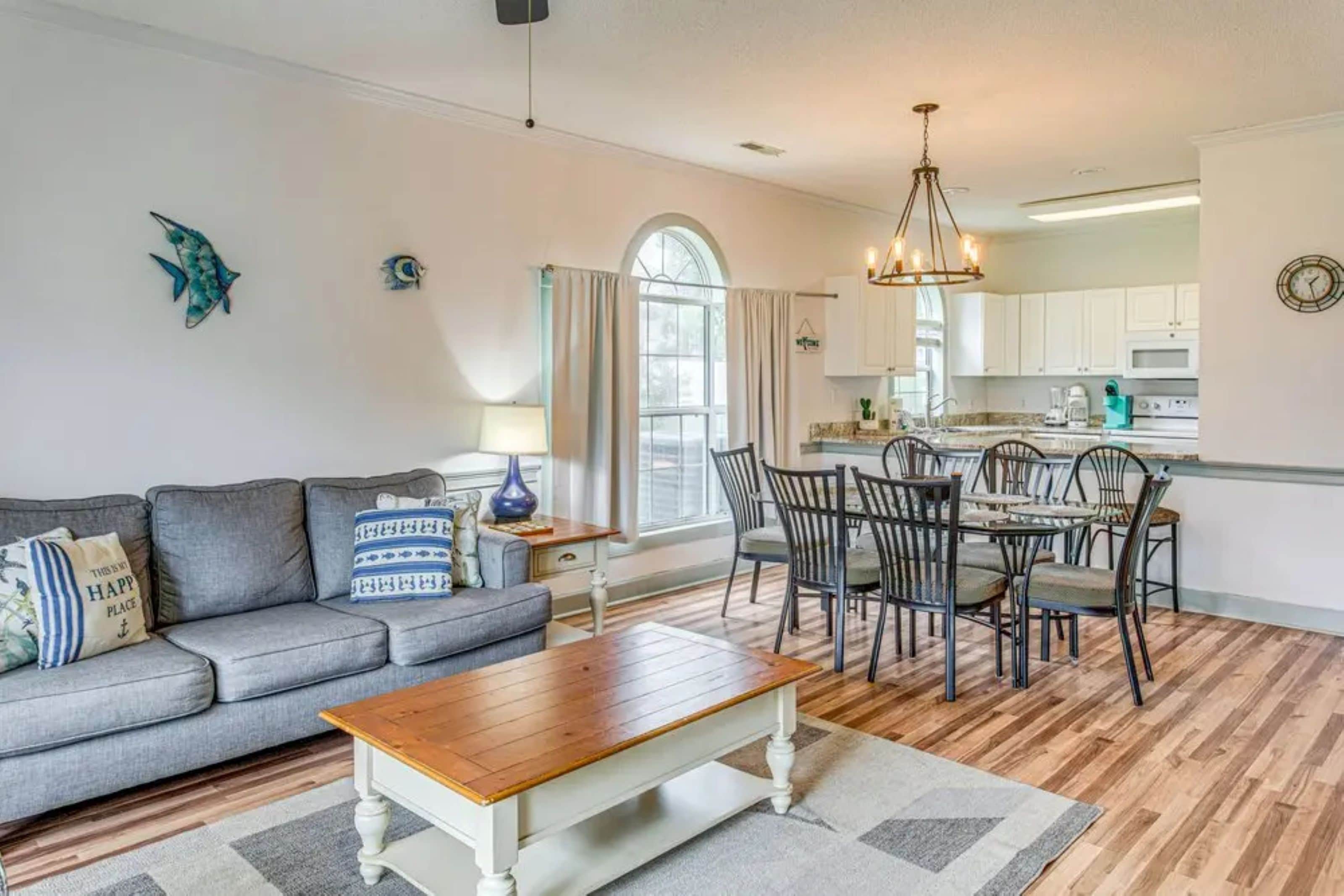 A living room with a sofa, coffee table, and dining area with chairs and a chandelier.