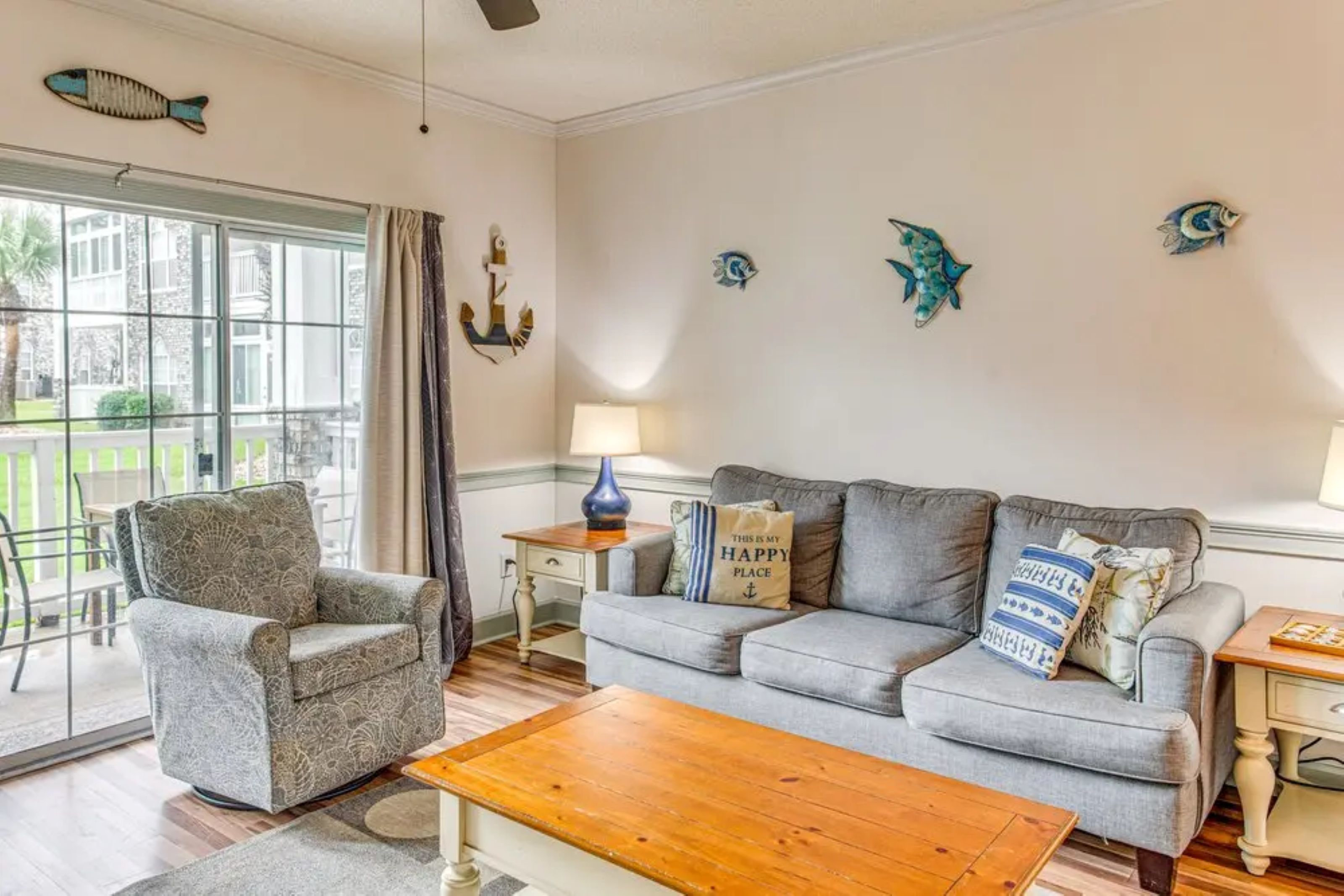 A living room with a grey sofa, a wooden coffee table, a patterned armchair, and decorative fish wall art.