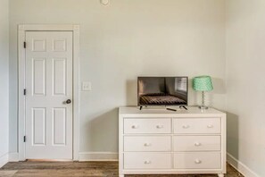 A white dresser with drawers, a television on top, and a green lamp beside it. - Myrtlewood Fall Special | Ground-Floor 2BR, Steps to Golf, Minutes to Beach (Myrtle Beach)