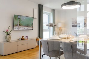 Ein moderner Essbereich mit einem Glastisch, der für eine Mahlzeit gedeckt ist, einem an der Wand montierten Fernseher und einer minimalistischen Einrichtung.
