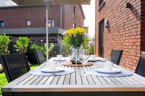 Une table à manger d’extérieur avec des assiettes blanches, des verres transparents et un vase rempli de fleurs jaunes.