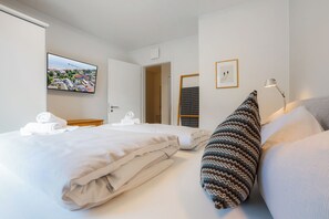 Ein Hotelzimmer mit zwei Betten, einem Fernseher, einem Schreibtisch und einer Tür zu einem weiteren Raum.