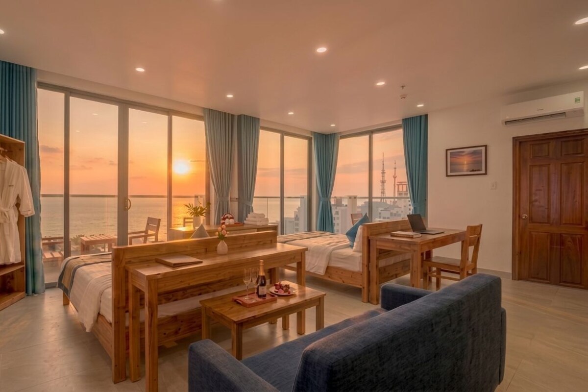 A hotel room with a bed, a desk, a sofa, a wooden wardrobe, and large windows with a city view.