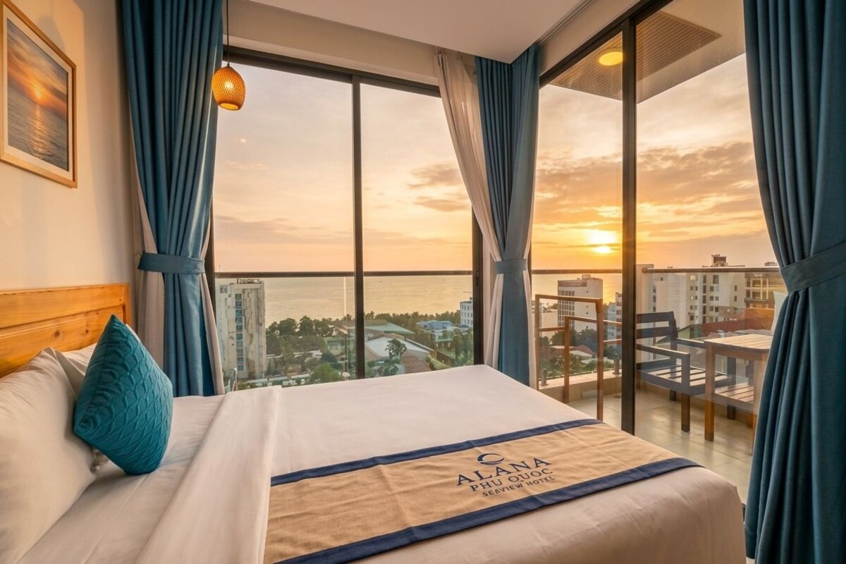 A hotel room with a bed, a view of the cityscape, and a balcony.