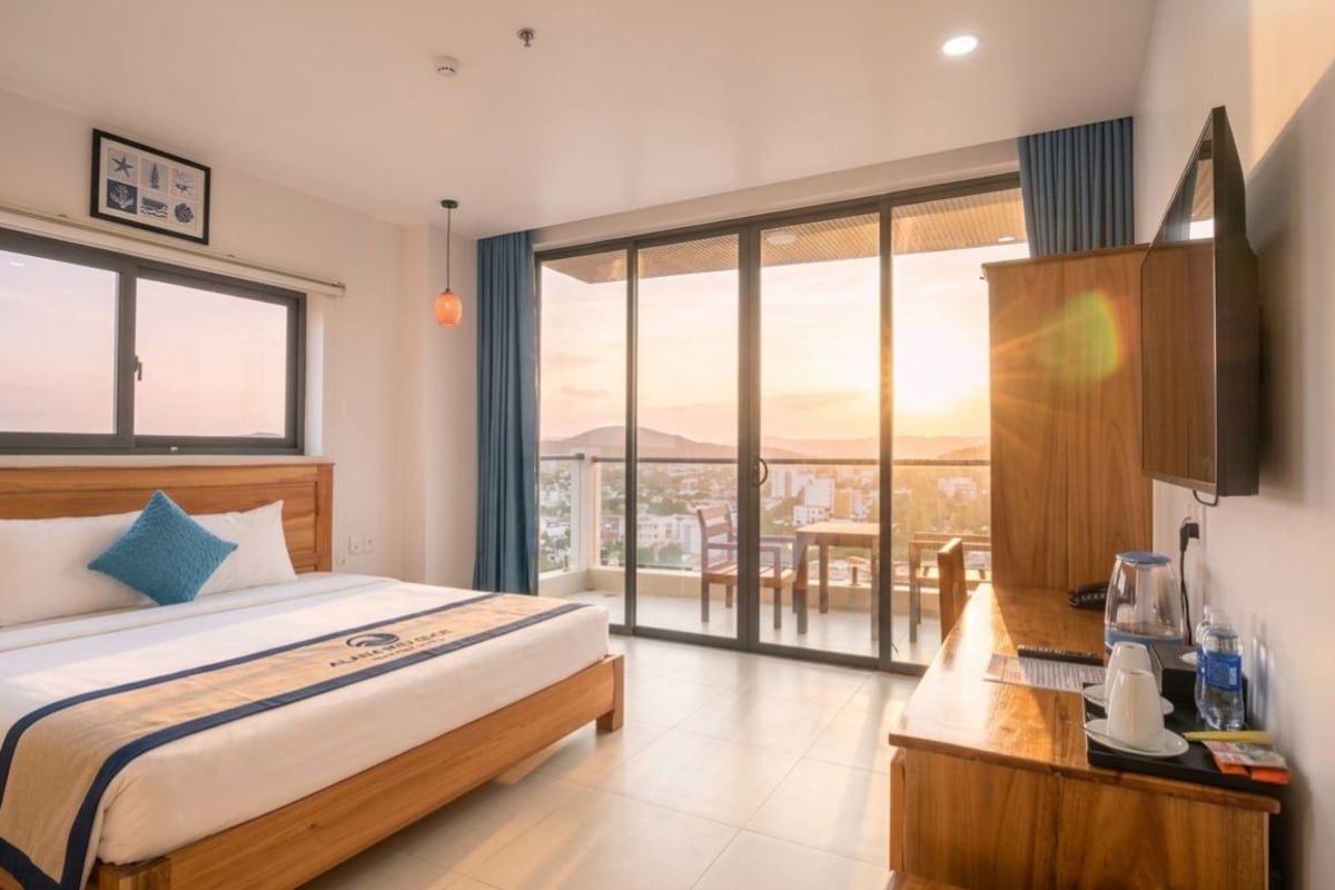 A hotel room with a bed, a desk, a flat-screen TV, and a large window with a city view.