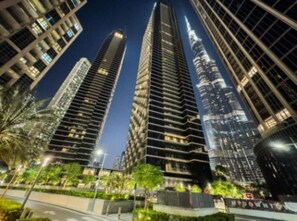Une vue nocturne de bâtiments modernes à étages élevés, dotés de façades en verre réfléchissant, et d’une rue urbaine bien éclairée.