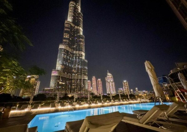 A nighttime view of a high-rise building with a pool area in the foreground. - Prestige 1-BR Address Opera | Pool + Parking (Dubai)