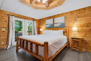 Ein hölzernes Bett mit weißer Bettwäsche, ein Nachttisch mit Lampe und zwei Bilder an der Wand.