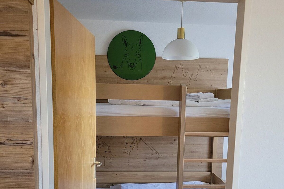 A bunk bed with a white lamp above it, a wooden door frame, and a wall with a circular green artwork.