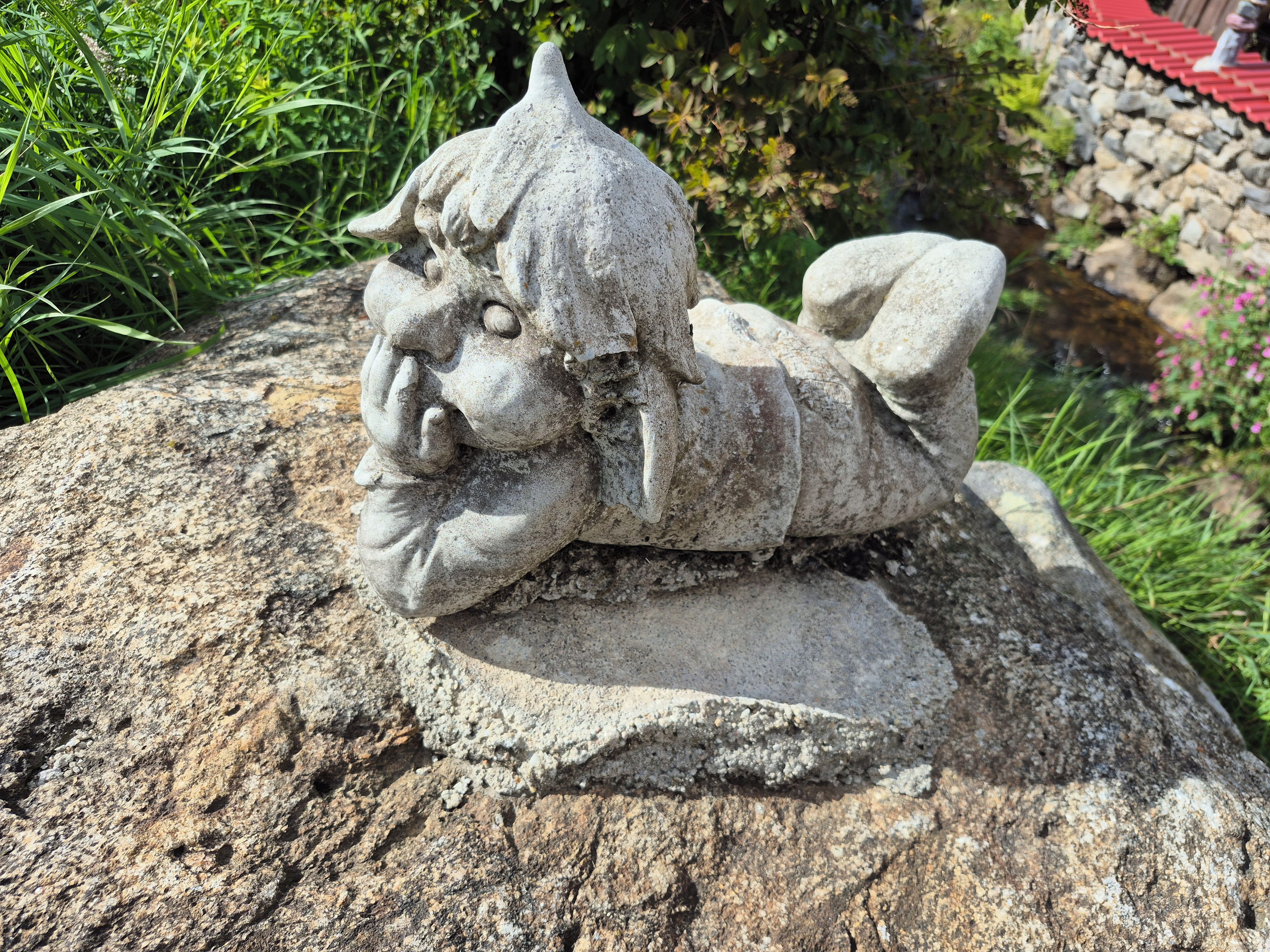 Une sculpture en pierre représentant une figure coiffée, allongée sur un rocher.